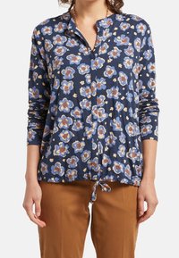 Blusa de manga larga azul marino con un patrón floral en azul claro, crema y marrón. Presenta un cuello con botones y un dobladillo ajustable.