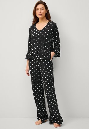 Zwart pyjama set bestaande uit een top met V-hals, een gerimpelde rand en lange mouwen, gecombineerd met bijpassende broeken versierd met witte hartpatronen.