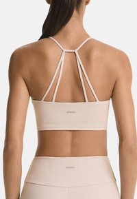 Light beige sports bra featuring thin crisscross straps at the back and a smooth texture, with the brand name “OYSHO” displayed.