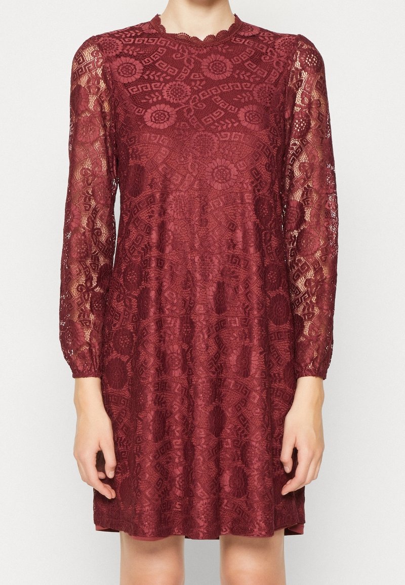Robe en dentelle bordeaux avec manches longues transparentes, motifs floraux et géométriques, col montant et bords de col festonnés.