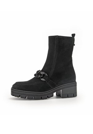 Schwarze Wildleder-Ankle Boots mit einer stabilen Sohle, die eine dekorative Kette auf der Vorderseite und eine Zuglasche auf der Rückseite für ein einfaches An- und Ausziehen besitzen.