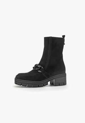 Schwarze Wildleder-Ankle Boots mit einer stabilen Sohle, die eine dekorative Kette auf der Vorderseite und eine Zuglasche auf der Rückseite für ein einfaches An- und Ausziehen besitzen.