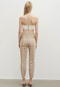 Top blanco sin tirantes con cremallera en la parte posterior, combinado con pantalones de cuadros beige de cintura alta, que presentan una textura suave y un diseño ajustado.