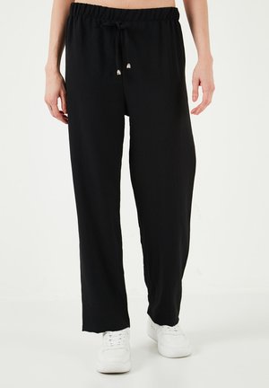 Black, lightweight, relaxed-fit pants with a drawstring waist and silver accented ends. Paired with white sneakers.