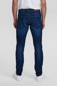 Temno modri denim hlače s ozkim krojem, petimi žepi in vidnimi šivi na zadnjih žepih. Gladka tekstura, minimalno zbledeli.