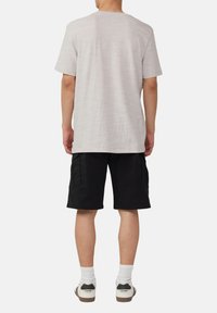 Jasnoszary t-shirt z krótkim rękawem o luźnym kroju, w zestawieniu z czarnymi szortami cargo. Strój uzupełniają białe skarpetki i sportowe buty.