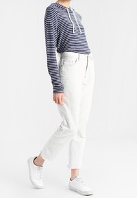 Marinfärgad och vit randig hoodie med snörning, tillsammans med vita cropped jeans med fransade fållar och vita sneakers.