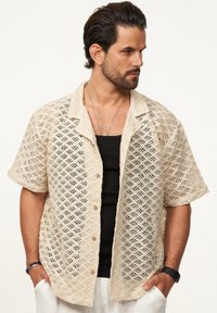 Kurzärmliges, gewebtes Hemd in Beige mit Rautenausschnitten, Knöpfen vorne und legerem Kragendesign. Strukturstoff.