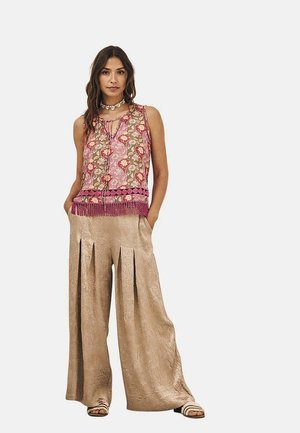 Top sin mangas con estampados florales y geométricos en rosa y verde, con flecos. Combinado con pantalones anchos de un beige claro con pliegues.