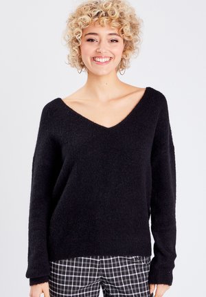Zwarte v-hals trui met een losse pasvorm, gemaakt van zacht, gestructureerd materiaal. Gecombineerd met zwart-witte geruite broek.