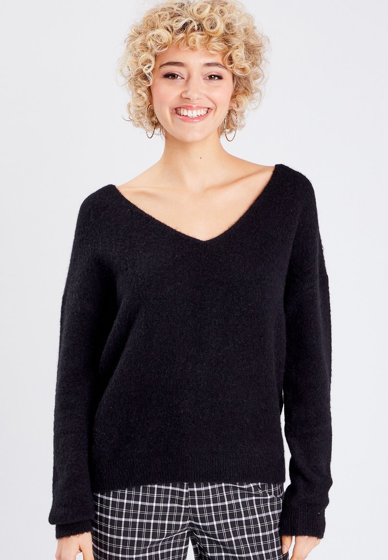 Sort v-hals sweater med en loose fit, lavet af blødt, struktureret materiale. Sammen med sort-hvidternede bukser.