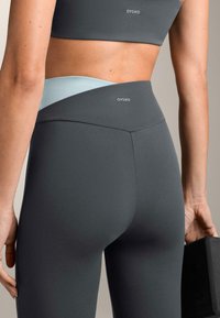 Colanți gri cu talie înaltă, cu un accent turcoaz, confecționați din material elastic. Logo-ul este vizibil pe talie.