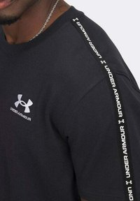 T-shirt in cotone nero con un piccolo logo bianco Under Armour sul petto e una striscia bianca con il marchio lungo la cucitura della spalla.