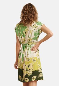 Floral dress featuring green and yellow leaf patterns, short sleeves, a tie waist, and a knee-length hemline. Smooth fabric texture.