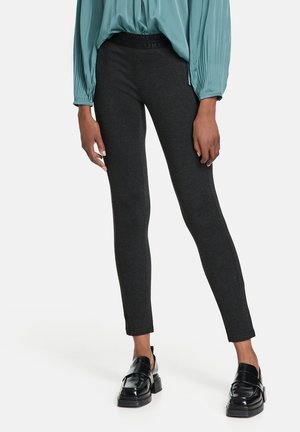 Leggings gris avec un design ajusté, fabriqués à partir d'un tissu lisse, présentant une taille haute et des jambes droites, associés à des mocassins noirs.