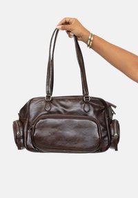 Bolso de cuero marrón con asas dobles, bolsillo frontal con cremallera y compartimentos laterales con cremallera. Textura suave, forma rectangular.