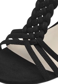 Svart mockask sandal med flätade remmar, öppen tå-design och en elegant, minimalistisk look med kontrast mellan beige och svart.