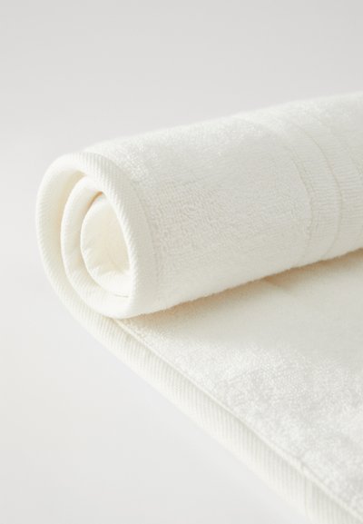 Λευκή βαμβακερή πετσέτα, τυλιγμένη με απαλή υφή, με χοντρό τελείωμα και διακριτικό υφαντό μοτίβο στην άκρη. Καθαρός, μινιμαλιστικός σχεδιασμός.