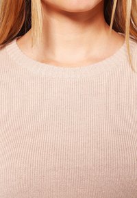 Pull rose clair côtelé avec un large col rond, présentant une texture douce et une coupe ajustée, mettant en valeur des motifs de tricot verticaux.