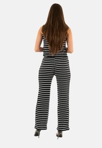 Combinaison à motifs noir et blanc avec des jambes larges, texture côtelée et corsage ajusté. Portée avec des talons aiguilles, vue de dos.