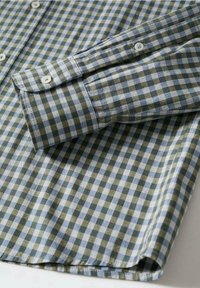 Poignet de chemise à manches longues avec fermeture par bouton, présentant un motif à carreaux verts et bleu clair sur tissu en coton.
