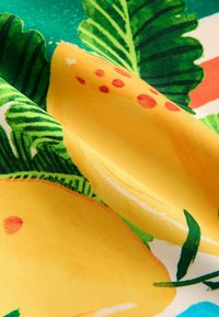 Tissu vibrant présentant de grands citrons jaunes avec des taches rouges et des feuilles vertes, sur un fond à motifs colorés.