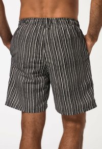 Bañadores de rayas en blanco y negro con cintura elástica, fabricados en tejido ligero y con bolsillos laterales, presentan un corte recto y una textura suave.