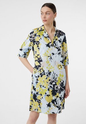 Robe fleuri en tissu bleu clair avec de grands motifs floraux jaunes et noirs, à manches courtes retroussées et col.