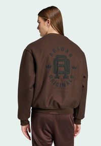 Brun sweatshirt med en afslappet pasform, der har et stort sort logo på ryggen, ribbede ærmer og talje. Blød struktur og afslappet stil.