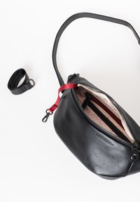 Zwarte leren crossbody tas met een gladde textuur, rode ritsaccenten en een stoffen interieur met een geometrisch patroon. Inclusief afneembare schouderband.