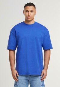 Royal blue bomulds oversized t-shirt med korte ærmer, rund hals, og en glat tekstur. Båret med lyse denim shorts.