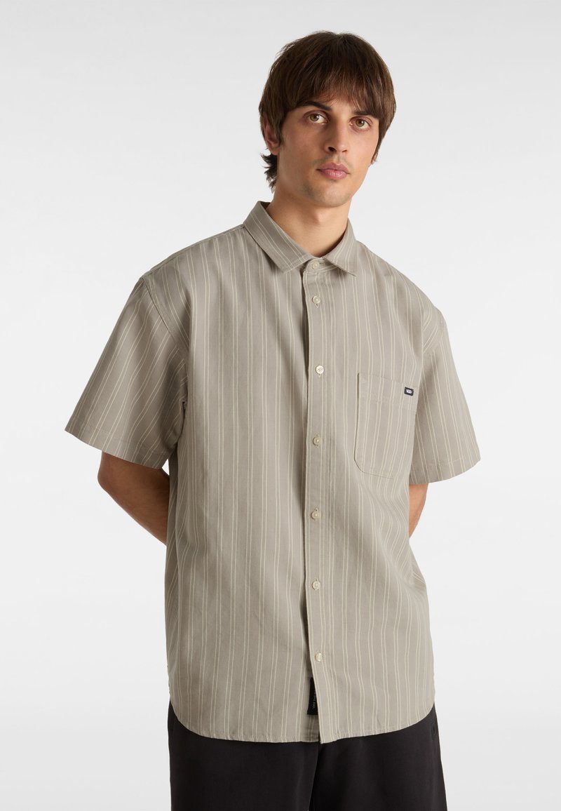 Kurzärmliges, kragenloses Shirt in hellbraun mit weißen vertikalen Streifen, ausgestattet mit einer Brusttasche und Knopfverschluss. Glatte Stofftextur.