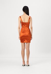 Robe mini en satin orange avec des bretelles larges, silhouette ajustée et fermeture à glissière au dos. Texture lisse et design épuré.