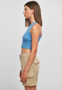 Blaues, geripptes Cropped-Top mit ärmellosem Design, kombiniert mit khakifarbigen Cargo-Shorts mit zwei Seitentaschen. Schlichte und figurbetonte Silhouette.