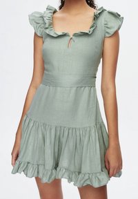 Hellgrünes Kleid aus Leinen, mit rüschierten kurzen Ärmeln, einem Schlüssel-ausschnitt am Hals und einem ausgestellten, rüschierten Saum.