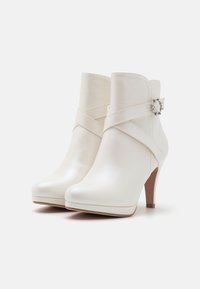 Botas de tobillo sintéticas blancas con textura suave, punta afilada, tacón alto y un diseño de correas cruzadas que presenta una hebilla decorativa de plata.