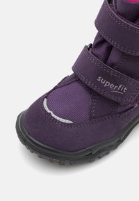 Chaussure pour enfants violette avec tige en textile, bandes Velcro et semelle en caoutchouc. Présente une finition lisse et des accents réfléchissants.
