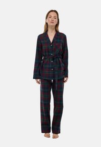 Ensemble de pyjama à carreaux en vert foncé et bordeaux. Tissu doux, chemise à boutons avec col et poche, pantalon ample avec taille élastique et cordon.