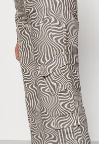 Calças de carga com um padrão ondulado preto e bege claro, feitas de tecido, com bolsos laterais e um design ajustado.