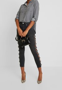 Camicia di denim grigia con maniche arrotolate, jeans neri a vita alta con dettagli a bottone laterali e una piccola borsa nera. Tacchi con stampa serpente.