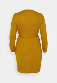 Robe jaune moutarde mi-longue avec des manches longues, un col rond et une ceinture en tissu à la taille, présentant une texture en maille lisse.