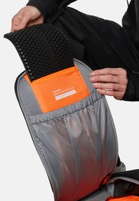 Schwarzer, strukturierter Rückenprotektor mit orangefarbigem Etikett, untergebracht in einer grauen Tasche. Glattes Material mit elastischem Besatz für einen sicheren Sitz.