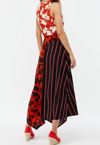 Czerwono-biały gorset w kwiaty przechodzi w czarną spódnicę z czerwonymi paskami. Ma wyższy przód i tył oraz czerwone sandały na koturnie.