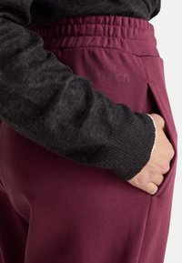 Burgunderfarbene Jogginghosen mit elastischem Bund und Seitentaschen, kombiniert mit einem dunkel strukturierten Sweater mit gerippten Bündchen.