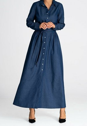 Frau trägt ein langärmeliges, dunkelblaues Maxikleid mit Knöpfen und einem gebundenen Taillengürtel sowie schwarze spitze Absätze.