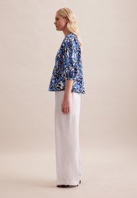 Bluse mit blau-weißer Blumenmusterung und Dreiviertelärmeln, kombiniert mit leichten, lockeren weißen Hosen. Strukturierter Stoff, lässiges Design.