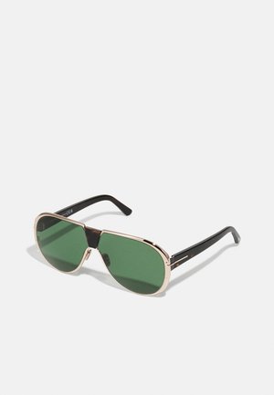Occhiali da sole con lenti verdi, montatura in metallo dorato e bracci in acetato nero. Presentano un design audace e angolare con un ponte che collega le lenti.
