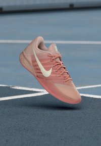 Nike'i spordijalats helepunases ja pehme virsiku toonis, millel on tekstureeritud pealmine osa, piklik kuju ja silmatorkav valge Swooshi logo.