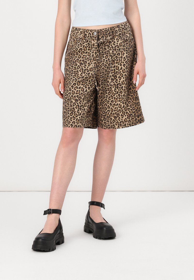 Shorts à imprimé léopard en marron et noir, offrant une coupe relax et des poches latérales. Associés à des chaussures noires à brides épaisses.