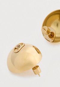 Σκουλαρίκια με στρας σε χρυσό τόνο που διαθέτουν απαλό, στρογγυλό σχέδιο. Περιλαμβάνουν ορατό κούμπωμα για ασφαλή στερέωση. Λαμπερή επιφάνεια με λογότυπο διακοσμητικό.